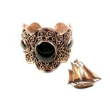 A silver brooch in the form of a boat and a white metal cuff set with large green stones,
