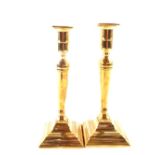 A pair of late 18th Century Adam style brass candlesticks on stepped square bases,