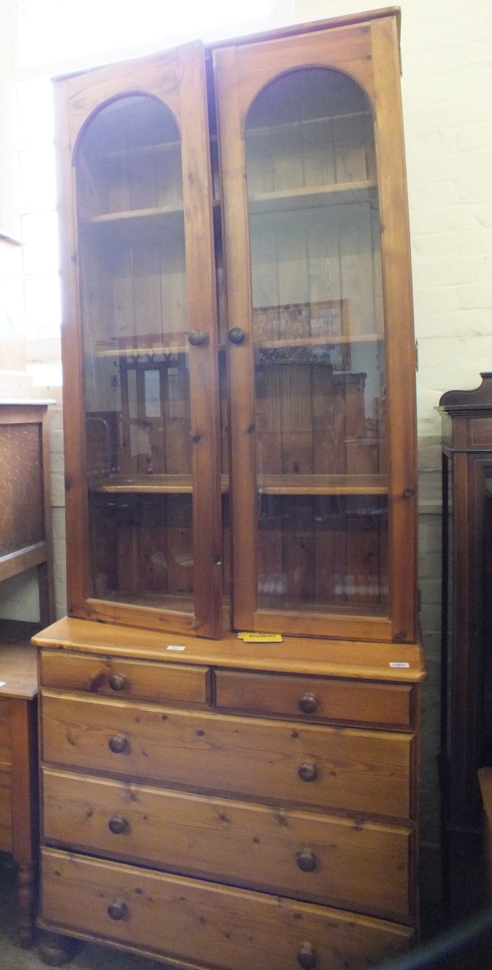 A modern pine glazed bookcase with chest of two short and three long drawers