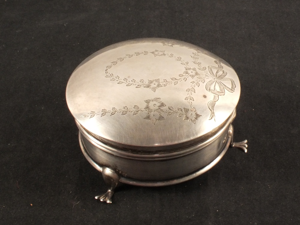 A circular silver trinket box with engraved floral detail to lid,