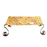 An Arts and Crafts rectangular embossed brass trivet on four scrolled iron legs,