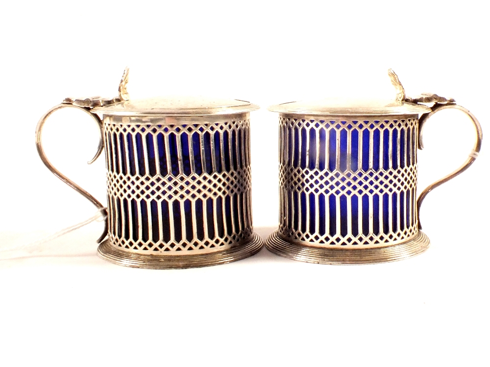 A matched pair of silver mustard pots with pierced design and crested lids,