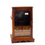 An Edwardian oak smokers cabinet with three drawers and bevelled glass door