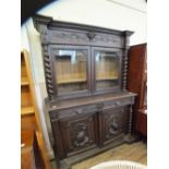 A substantial carved oak bookcase sideboard with two glazed doors flanked by barley twist columns