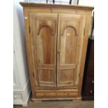 A stripped pine two door wardrobe with single drawer below