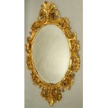 A large Continental giltwood and gesso oval wall mirror, the frame elaborately carved with