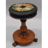 A Victorian mahogany revolving piano stool, the padded top inset with a woolwork floral panel, on
