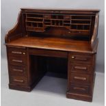 An early 20thC oak roll top desk, with eight drawers to each pedestal, flanking a central drawer,