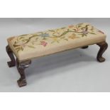 An early 20thC walnut fender type stool, with a crewelwork padded seat, on shell carved cabriole