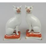 A pair of 19thC Staffordshire pottery cats, each seated on a coloured cushion, with gold tassels