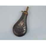 A bloomed copper and brass powder flask, decorated with a cannon, flags, etc.