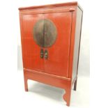 An oriental red painted hardwood cabinet, with two doors, each with engraved brass mounts, enclosing