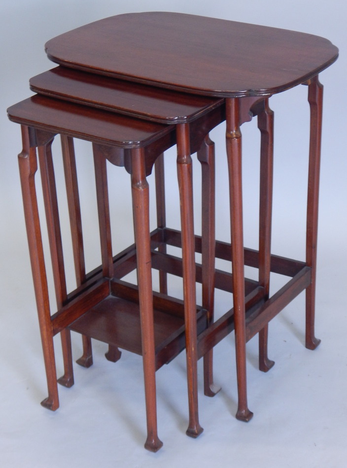 A nest of three Edwardian mahogany tables, each with a shaped top on turned legs and square feet,