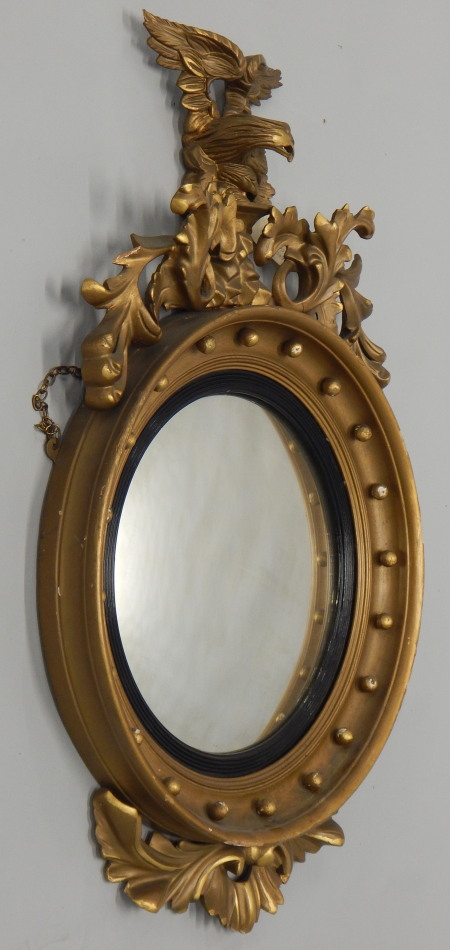 A Regency giltwood and gesso convex wall mirror, mounted with an eagle and foliate scroll crest, the