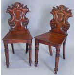 A pair of Victorian mahogany hall chairs, each with a shaped back carved with a central shield on