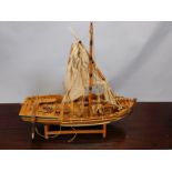 A scale model of a single masted sailing ship, part painted in yellow and blue, on a wooden stand,