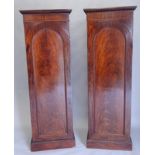 A pair of figured mahogany pedestal wardrobes, each with a carved cornice and a single door with