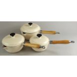 Three Le Creuset style cream enamel pans, each with turned wooden handles