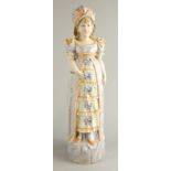 A large German bisque porcelain figure of a lady, wearing a purple dress with frilled skirt, etc.,