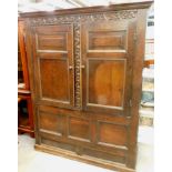 An oak cupboard, the top with a moulded cornice, a leaf carved frieze and two panelled doors