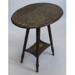 A Burmese type two tier occasional table, the oval top carved with entwined serpents, etc., on