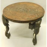 An oriental hardwood table, the carved circular top on elephant shaped supports, each with bone