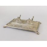 An early 20thC metal inkstand, with two lidded wells, a pen rest, on paw feet, 26cm wide.