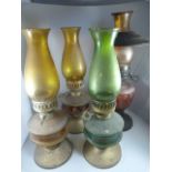 Four oil lamps, two with amber glass well, one with cranberry glass well and one green