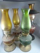 Four oil lamps, two with amber glass well, one with cranberry glass well and one green