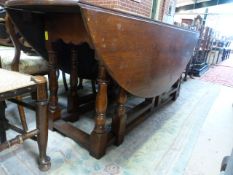 An oak drop leaf gate legged coffin table with oval top on turned Legs.