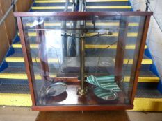 An antique set of Chemist weighing scales surrounded by wooden and glass case