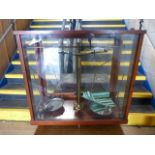 An antique set of Chemist weighing scales surrounded by wooden and glass case