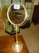 An early 20th century brass shaving mirror having a double sided swivel mirror raised on a