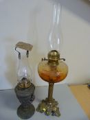 Two period metal based oil lamps with brass fittings and glass chimneys - One with Amber glass well