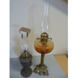 Two period metal based oil lamps with brass fittings and glass chimneys - One with Amber glass well