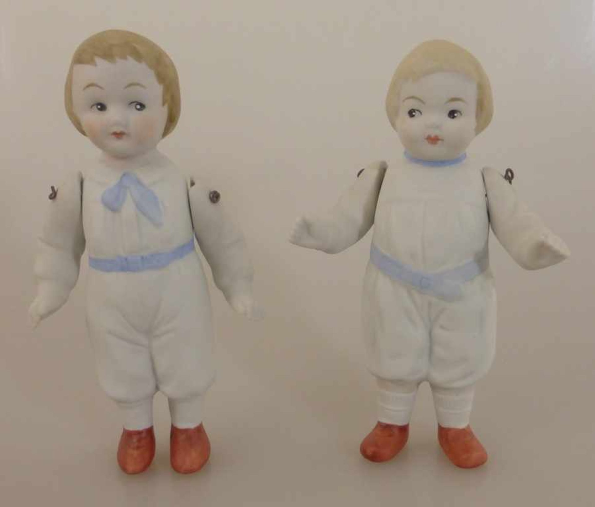2 Puppen Bisquitporzellan, 20.Jh., bewegliche Arme, h. 12,5cm, eine Puppe am Arm min. best.