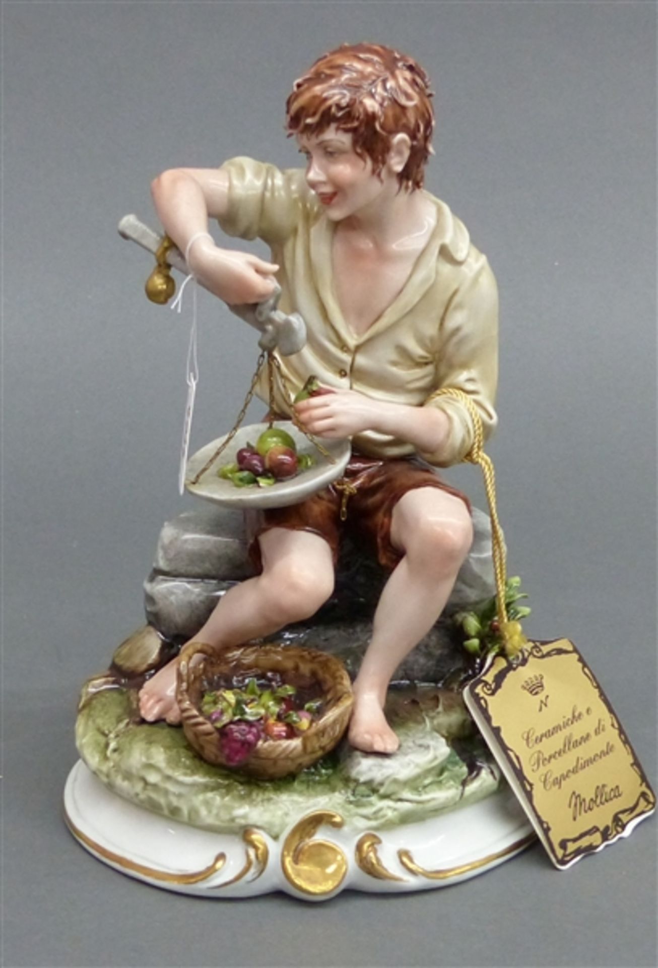 Porzellanskulptur Capodimonte, bemalt, sitzender Junge mit Obstkorb und Waage, Neapel, h 22 cm,