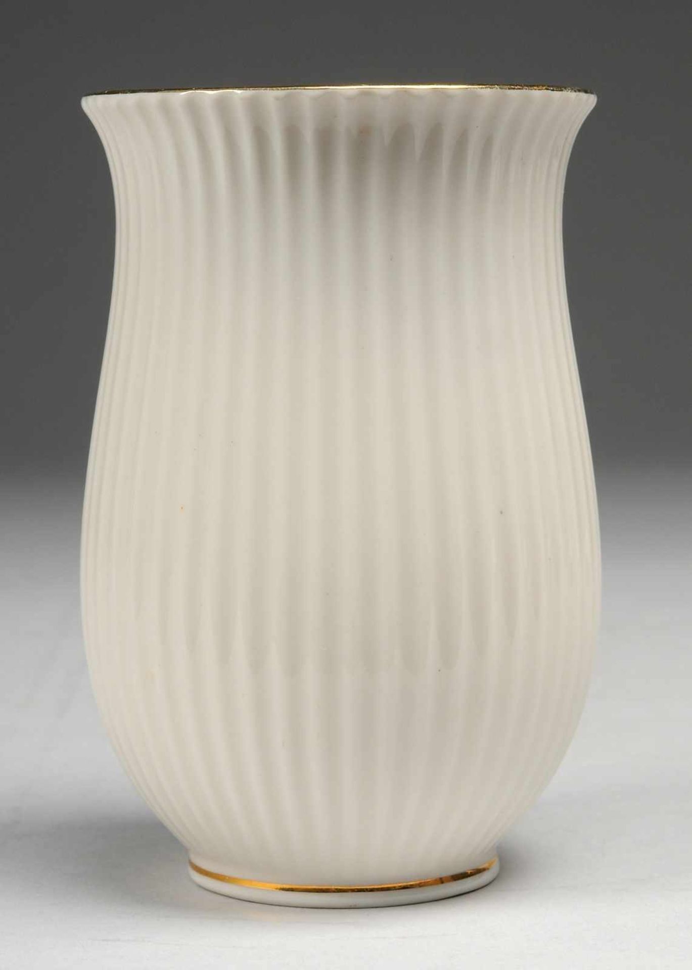 Vase Weiß, glasiert. L. geschwungene Form mit vertikalem Linienreliefdekor. Goldränder. Firmenmarke.