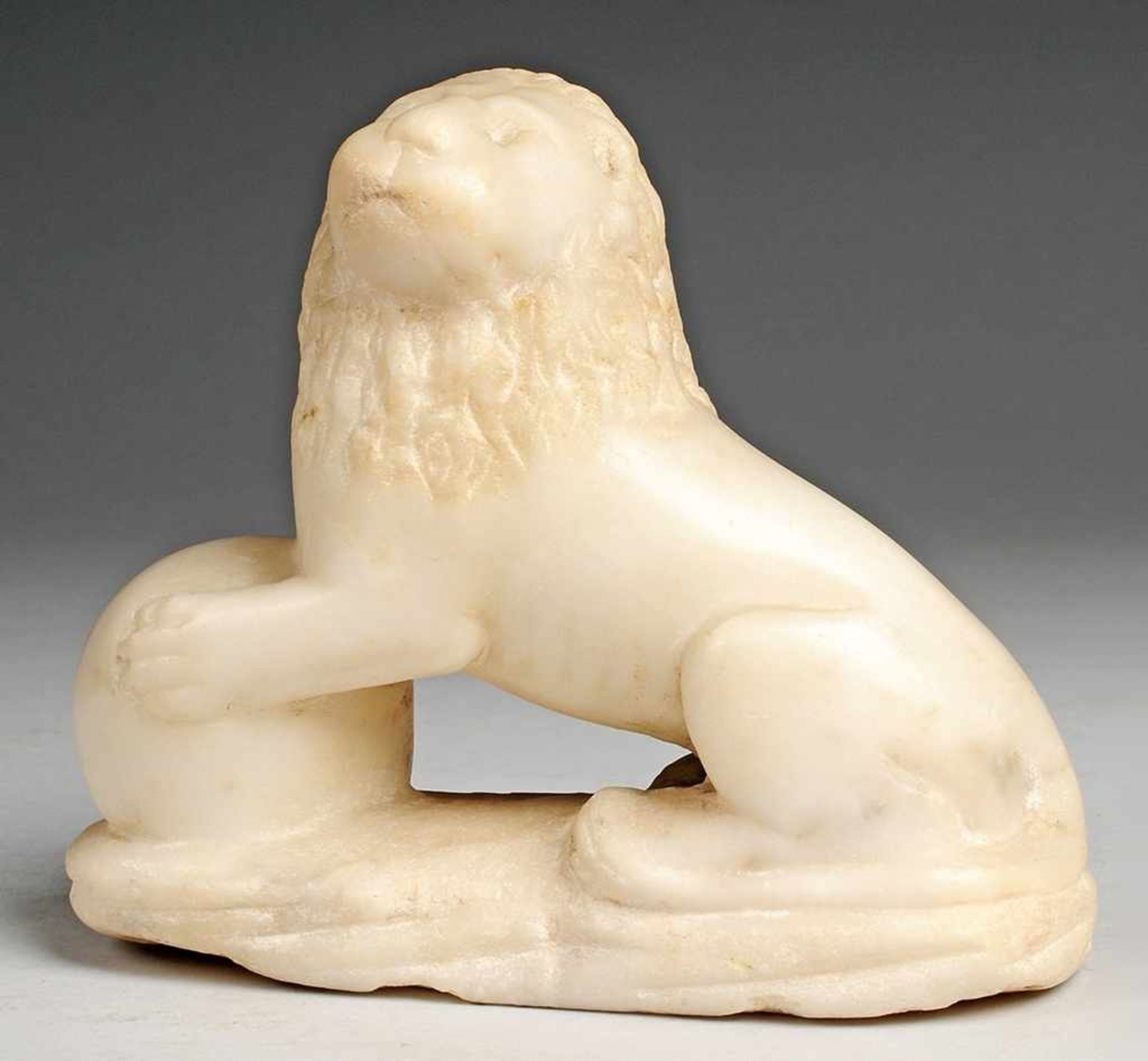 Wächterlöwe Weißer Marmor. Auf ovaler Plinthe Figur eines auf den Hinterläufen sitzenden Löwen mit