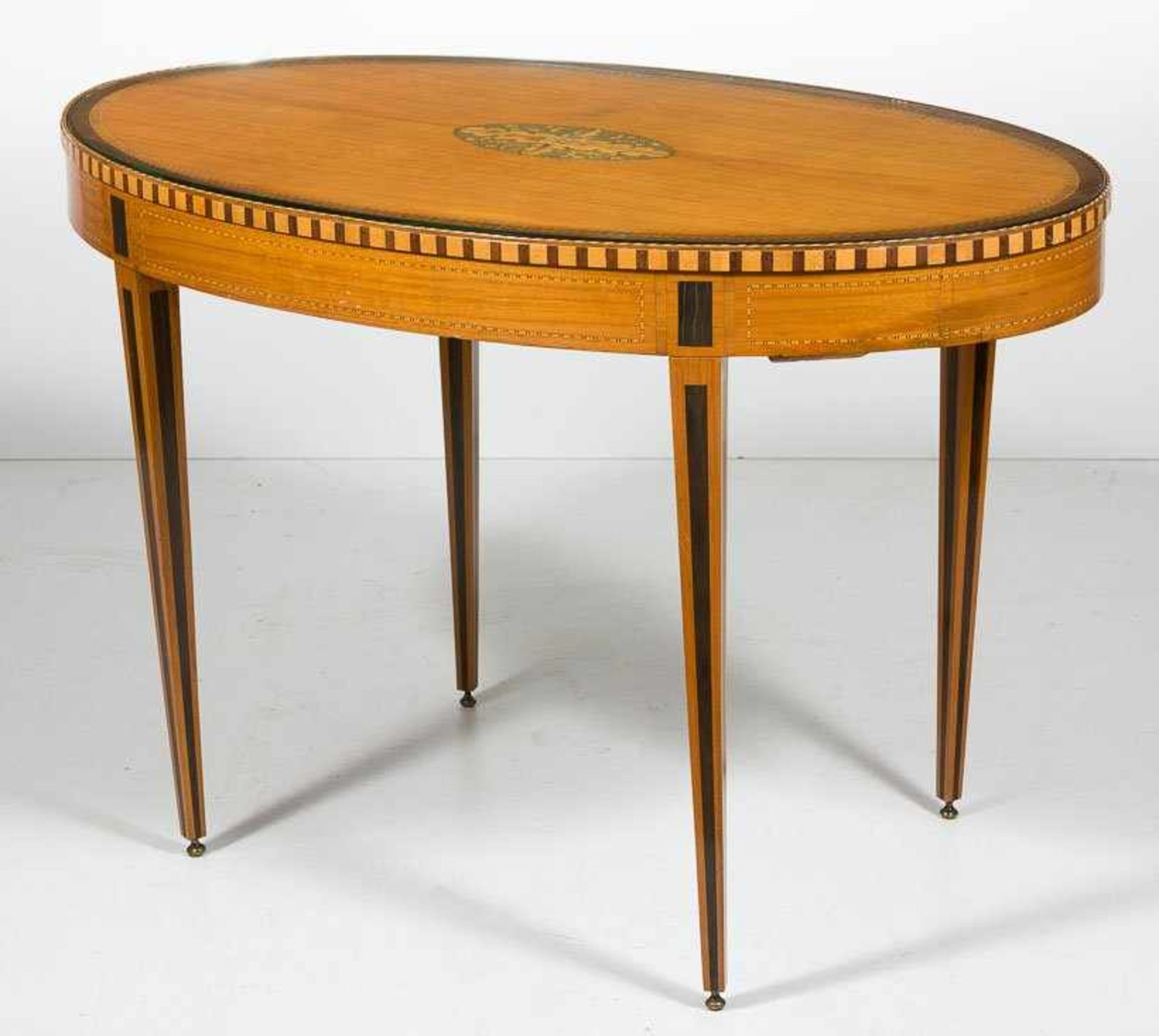 Ovaler Tisch im Sheraton-Stil. Satinholz und div. Einlagehölzer, gefriest und gefeldert. In der