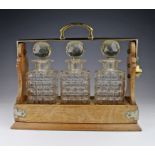 Oak and brass tantalus containing three cut glass decanters with stoppers (a few chips to stoppers),
