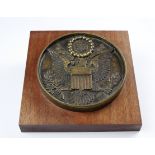 Bronze plaque depicting the United States of America (USA) coat of arms, mounted on a square piece