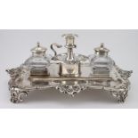 Silver desk stand with an ornate border raised on four feet, containing two glass inkwells with