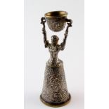 White metal and brass wager cup, depicting a lady holding a cup aloft, length 13cm approx.