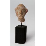 Roman grotesque male head in terracotta, c.40mm in high, set on a wooden stand, painted in matt