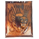 An early 20th century African embossed copper panel, depicting an African mask and weapons