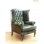 A green leather wing back armchair with button back