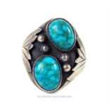 A silver and twin cabachon turquoise stone set ring, the engraved silver mounts cast in the form