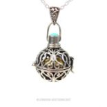 A pierced silver pendant with a brass ball inside topped with turquoise