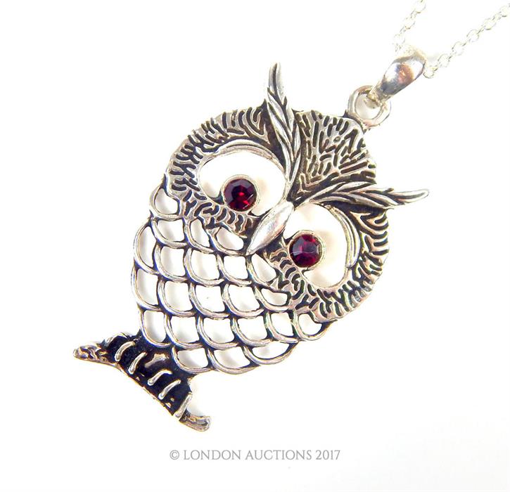 A silver owl shaped pendant necklace with ruby eyes and silver chain